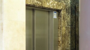 Een metalen lift met een bedieningspaneel, voor een marmeren wand.