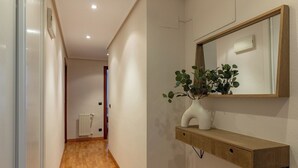 Een hal met houten vloer, een witte radiator, een spiegel aan de muur en een plankje met een plant.
