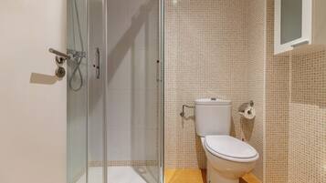 A bathroom with a toilet, a shower enclosure, and a mirror.