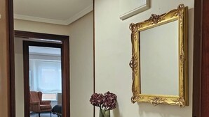 A hallway with a marble floor, a dark wooden console table with a vase of flowers, a large ornate mirror, and a ceiling light. - Apartment AH2 by Gestión House. VUT-6514-AS (Noreña)