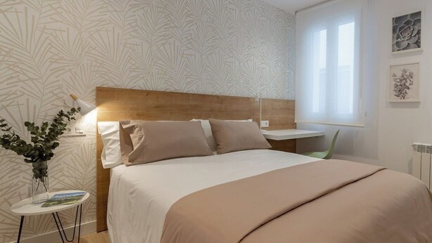 Un dormitorio con cama, mesita de noche, lámpara y ventana con vistas.