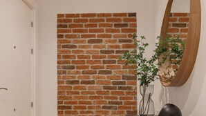 Una habitación con pared de ladrillo, un espejo redondo, una lámpara negra y un florero con planta.