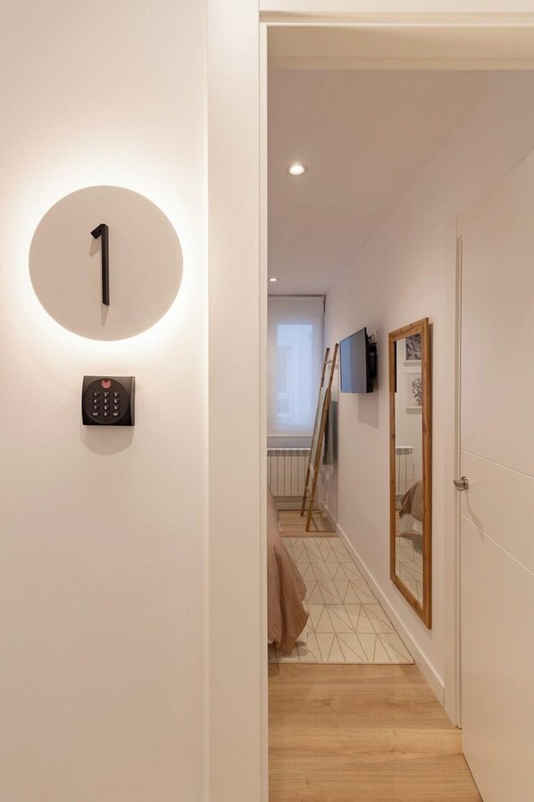 Un couloir avec un panneau portant le chiffre 1, fixé au mur, un clavier de sécurité, un plancher en bois, un miroir et un téléviseur.