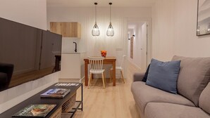 Una sala de estar moderna con un televisor de pantalla plana, una mesa de comedor de madera con sillas y un sofá con un cojín azul.