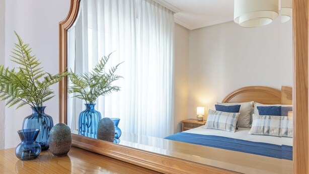Une chambre à coucher comprenant un lit, une table de chevet, une lampe et des objets décoratifs, notamment des vases et un miroir.