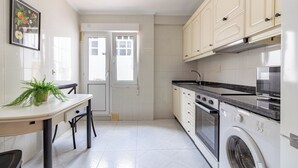 Une cuisine compacte avec des meubles blancs, un four encastré, un lave-linge et un coin repas comprenant une table et des chaises.