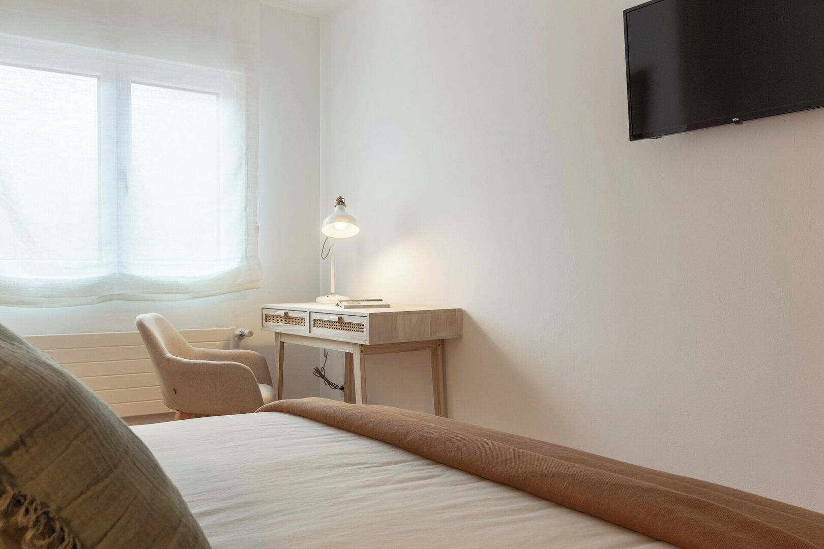 Ein Schlafzimmer mit Bett, Schreibtisch mit Lampe, Stuhl und Fernseher an der Wand.