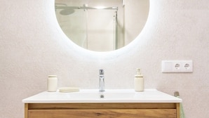 A bathroom with a round mirror, a wooden vanity, a sink, and a shower. - Asturias holidays by Gestión house 3 (Noreña)