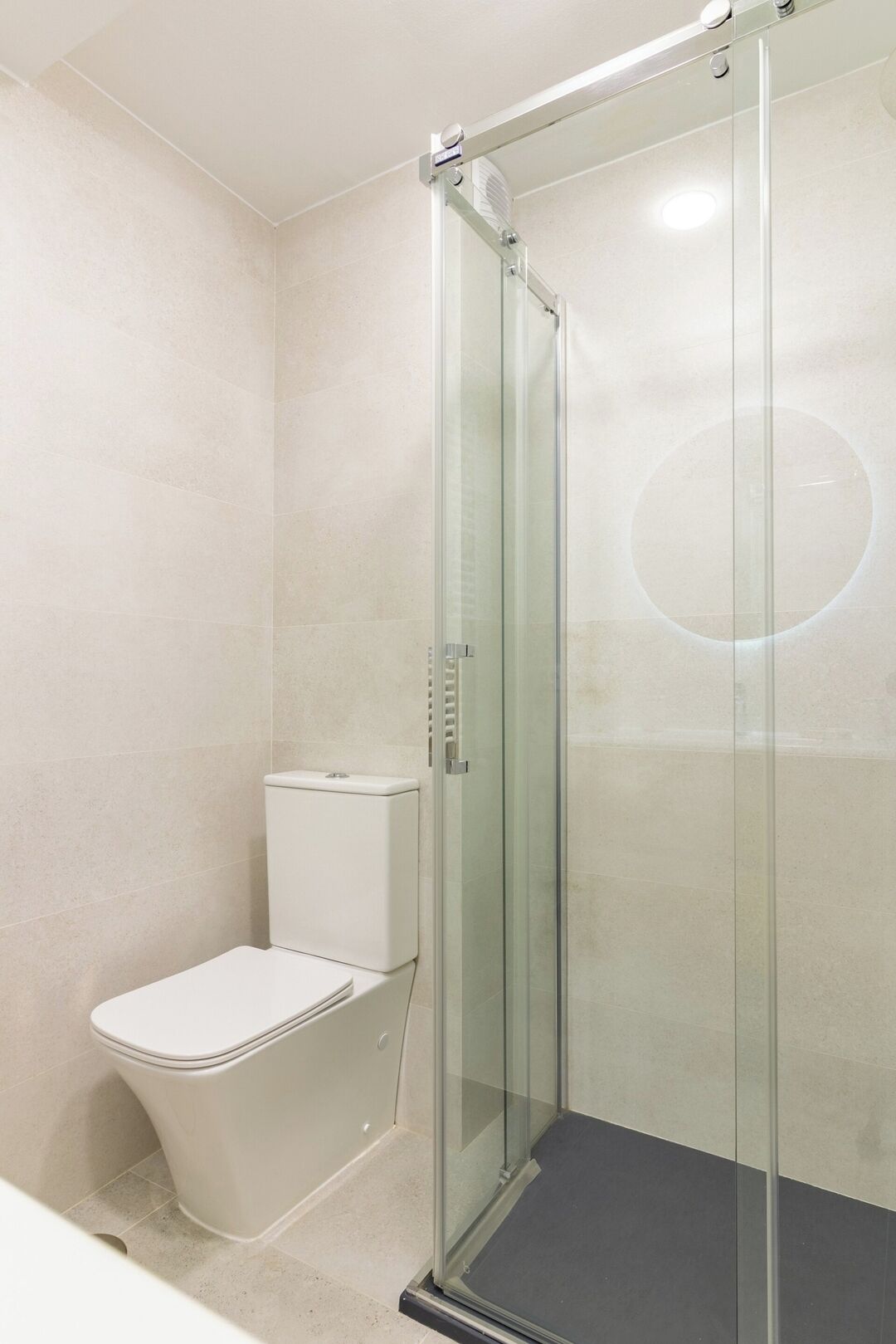 A modern bathroom with a glass-enclosed shower, a toilet, and a tiled floor.