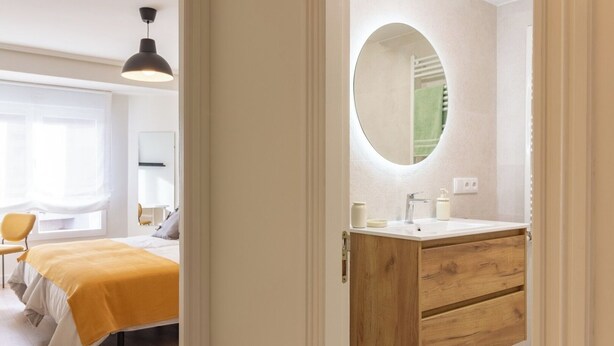 A hotel room with a bed, a bedside table, a mirror, a wooden vanity with a sink, and a window with curtains. - Asturias holidays by Gestión house 3 (Noreña)