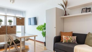 Ein modernes Wohnzimmer mit grauem Sofa, einem Holzesstisch und einem an der Wand montierten Fernseher.