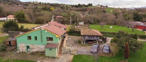 A rural house with a green exterior and a red roof, surrounded by a grassy yard and a small garden.