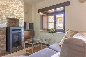 Un salon avec un mur en pierre, une cheminée, une table basse en verre, un canapé et une fenêtre donnant sur un beau paysage.