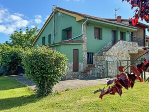 Une maison à deux étages avec un escalier en pierre, une façade verte et un petit jardin.