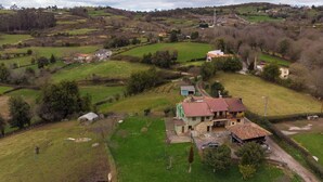 A rural landscape with a house featuring a red-tiled roof, surrounded by green fields and scattered trees. - AH Townhouse "La Casina de Cués". VV-1762-AS (Asturias)