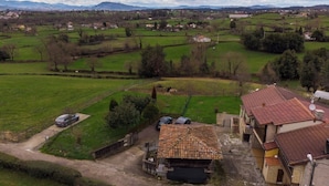 A rural landscape with a house featuring a tiled roof, a fenced yard, and a car parked outside. - AH Townhouse "La Casina de Cués". VV-1762-AS (Asturias)