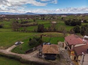 A rural landscape with a house featuring a tiled roof, a fenced yard, and a car parked outside. - AH Townhouse "La Casina de Cués". VV-1762-AS (Asturias)