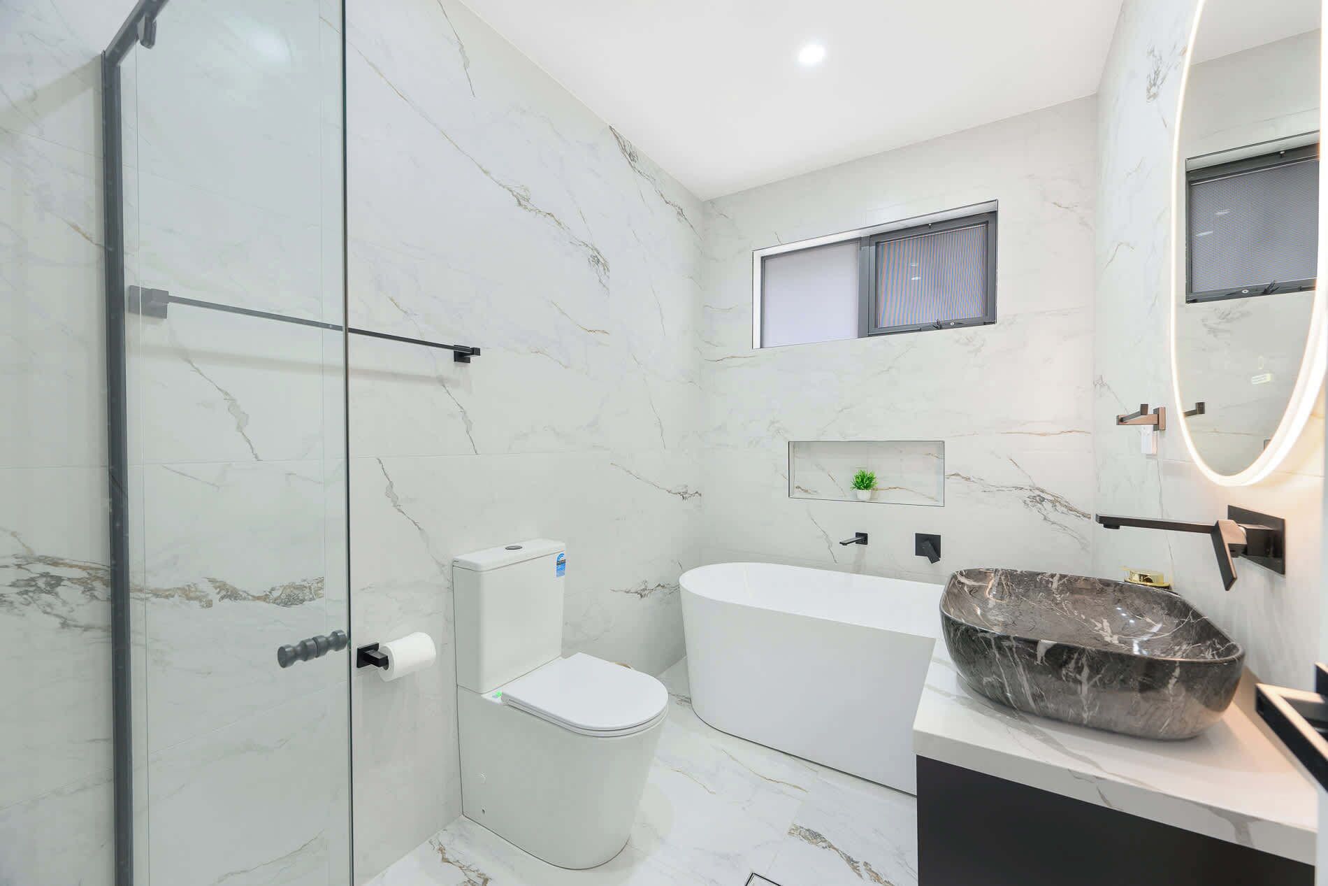 Ein modernes Badezimmer mit Duschkabine aus Glas, Toilette, Badewanne und Marmorwaschbecken mit Schale.