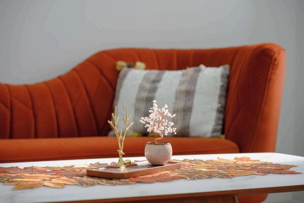 A cozy living room with a red sofa, a small table with a decorative bowl and branches, and a patterned rug.