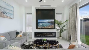 A modern living room with a grey sofa, a black and gold coffee table, a large flat-screen TV, and a potted plant.