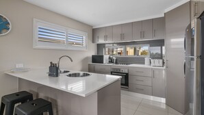 Una cocina moderna con armarios grises, encimera blanca, horno integrado y refrigerador de acero inoxidable.