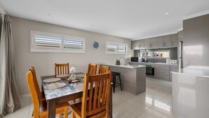 Una cocina moderna con una isla central, un comedor con sillas y mesa de madera, y vistas al exterior a través de amplios ventanales.