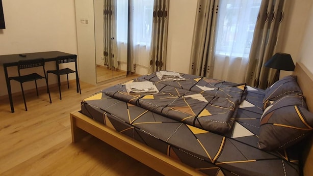A bedroom with a bed, a desk, chairs, a mirror, and a lamp.