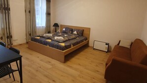 A bedroom with a bed, a table, a chair, a sofa, and a heater.
