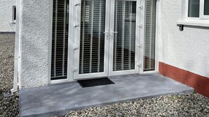 A building with a textured exterior, a concrete patio, and a set of double doors with louvered glass panels. - Studio Apartment in Londonderry (Londonderry)