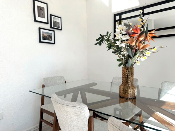 Un coin repas moderne avec une table en verre, quatre chaises et un vase rempli de fleurs.