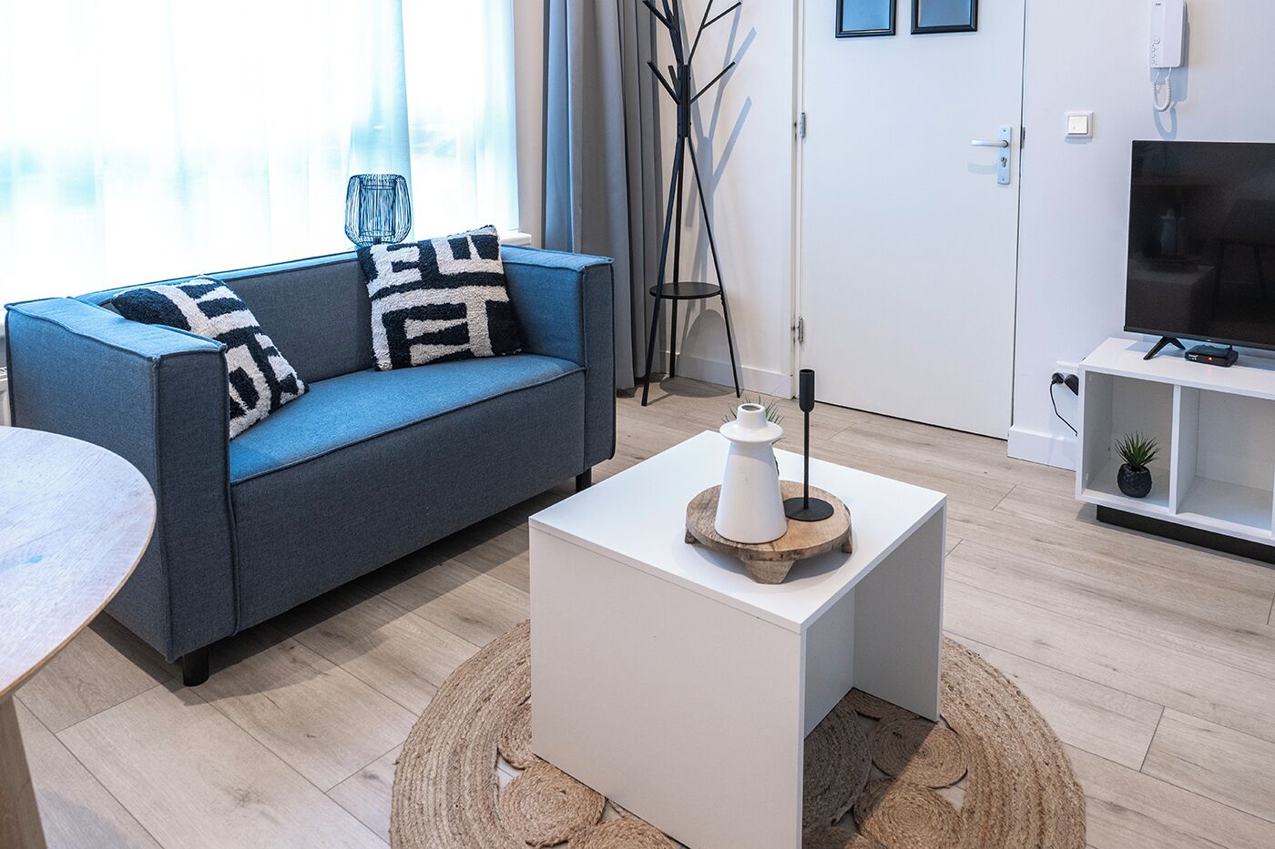 Un salon moderne avec un canapé bleu, une table basse blanche et un meuble pour la télévision agrémenté d’une plante.