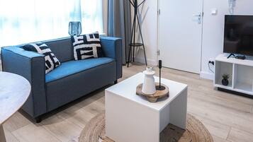 Un salon moderne avec un canapé bleu, une table basse blanche et un meuble pour la télévision agrémenté d’une plante.