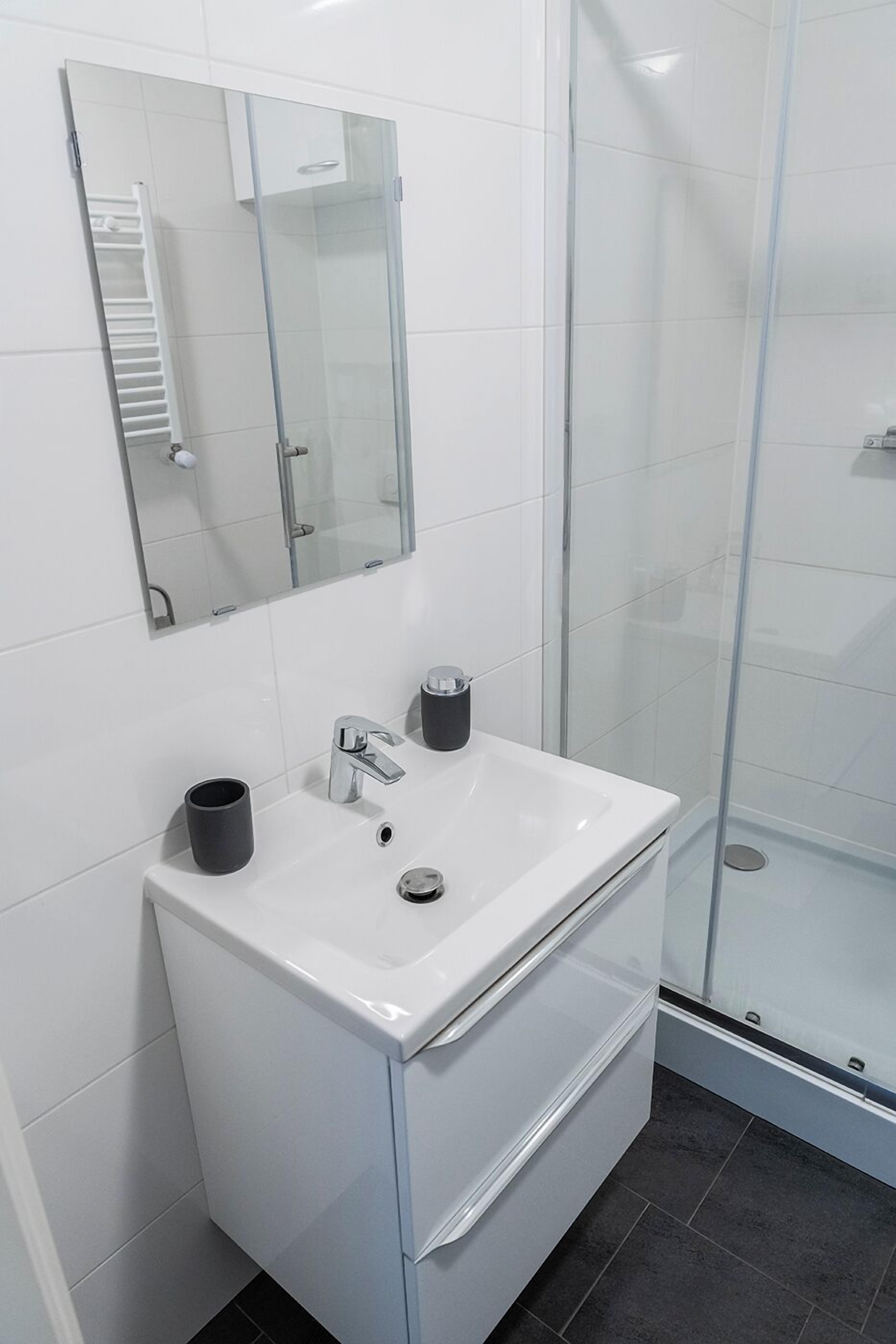Une salle de bain moderne avec un lavabo blanc, un miroir et une cabine de douche en verre.