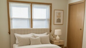 A bedroom with a bed, a nightstand, a lamp, a ceiling fan, and a door.