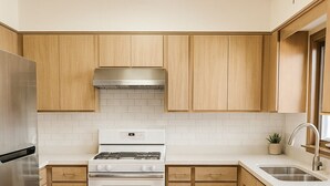 A modern kitchen with wooden cabinets, a stainless steel refrigerator, a white stove, and a dishwasher.