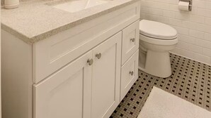 A modern bathroom with a double sink vanity, a toilet, and a large mirror with wall-mounted lights.