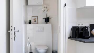 Een moderne keuken met witte kasten, een zwart aanrecht en een zichtbare prullenbak.