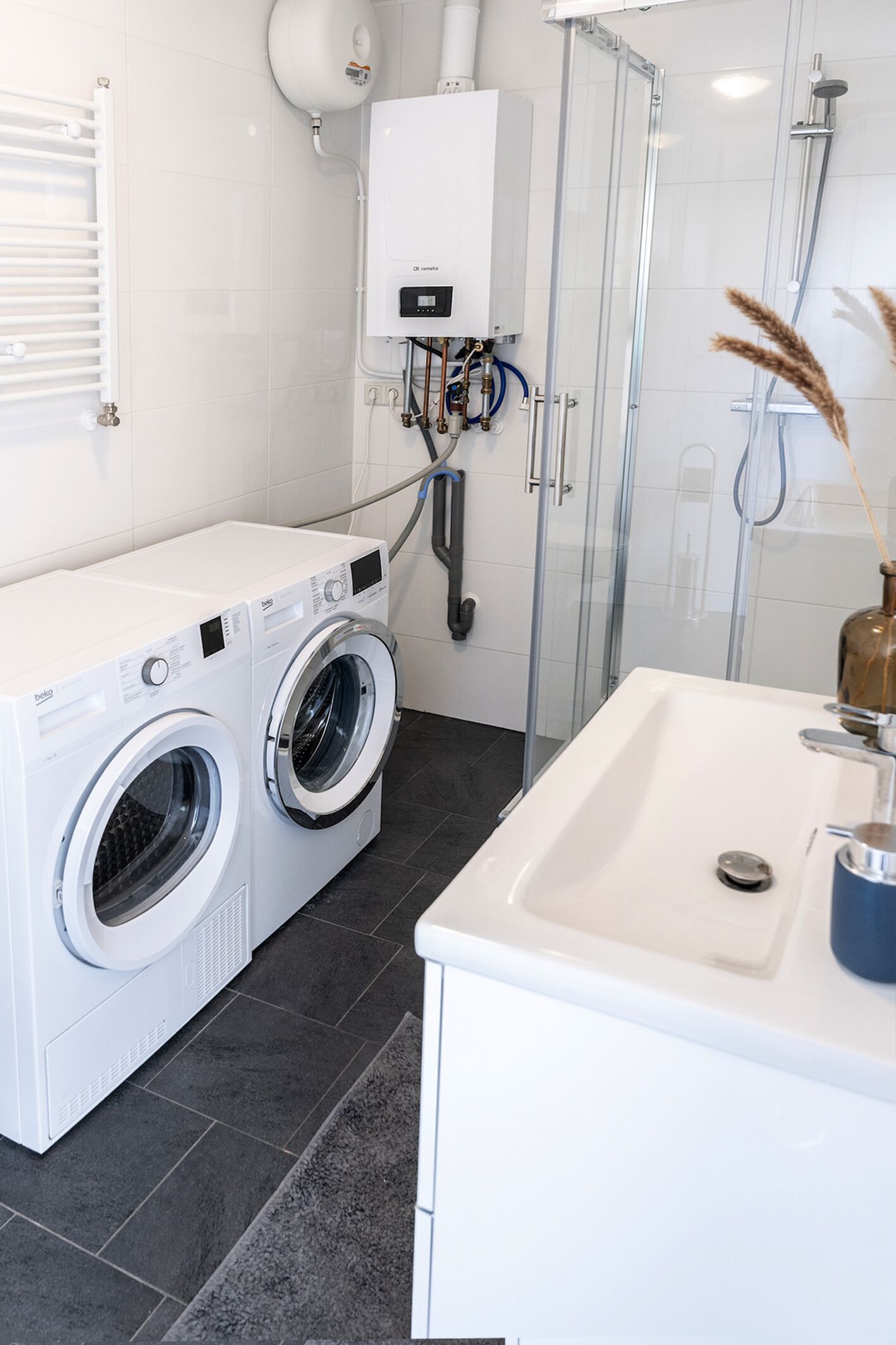 Ein modernes Badezimmer mit integrierter Waschmaschine und Trockner, einer Duschkabine aus Glas und einem weißen Waschbecken.
