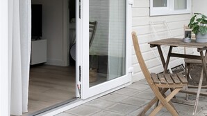 A patio with a wooden table and chairs, a sliding glass door leading to an interior room, and a potted plant on the table.