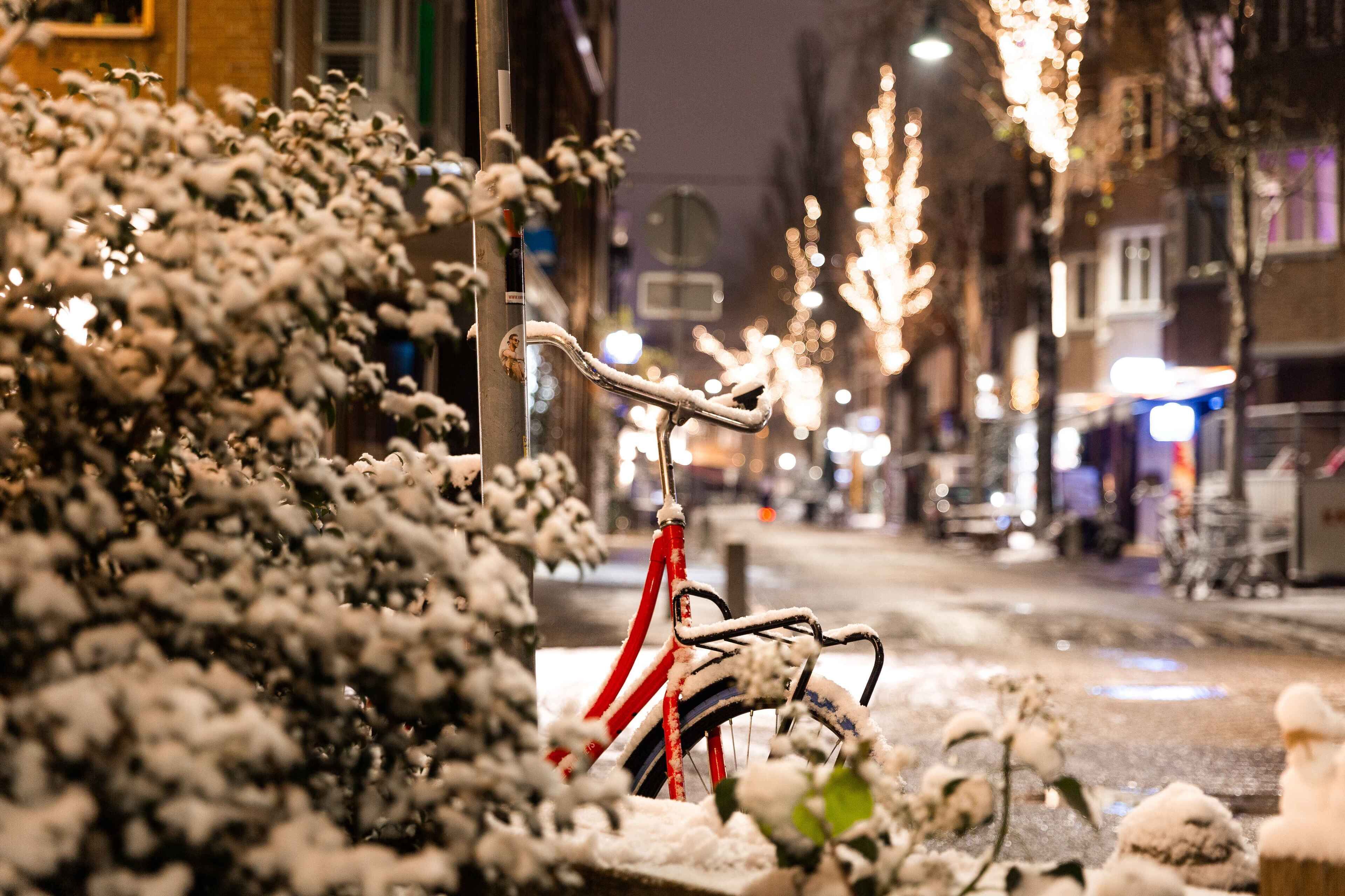 Een fiets die tegen een paal leunt, met een besneeuwde straat op de achtergrond.