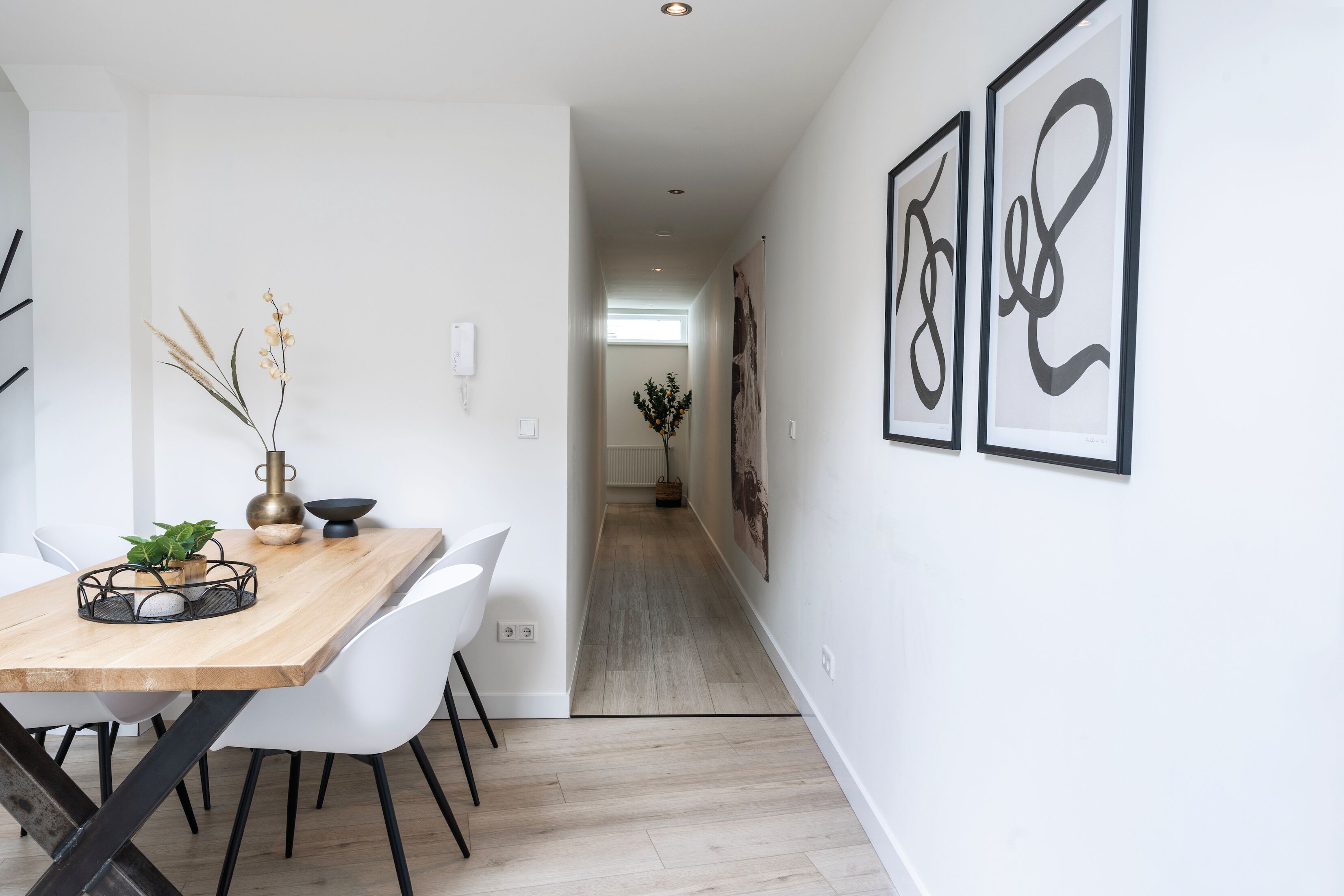 Un intérieur moderne avec une table à manger en bois, des chaises blanches et des œuvres d’art abstraites accrochées aux murs.