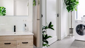 A modern bathroom with a wooden vanity, a large mirror, and a washing machine in the background.