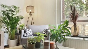 Un soggiorno moderno con un divano grigio, diverse piante in vaso, una lampada da terra e un vassoio con candele.