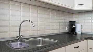 A kitchen with a double sink, white cabinets, a coffee maker, and a kettle.