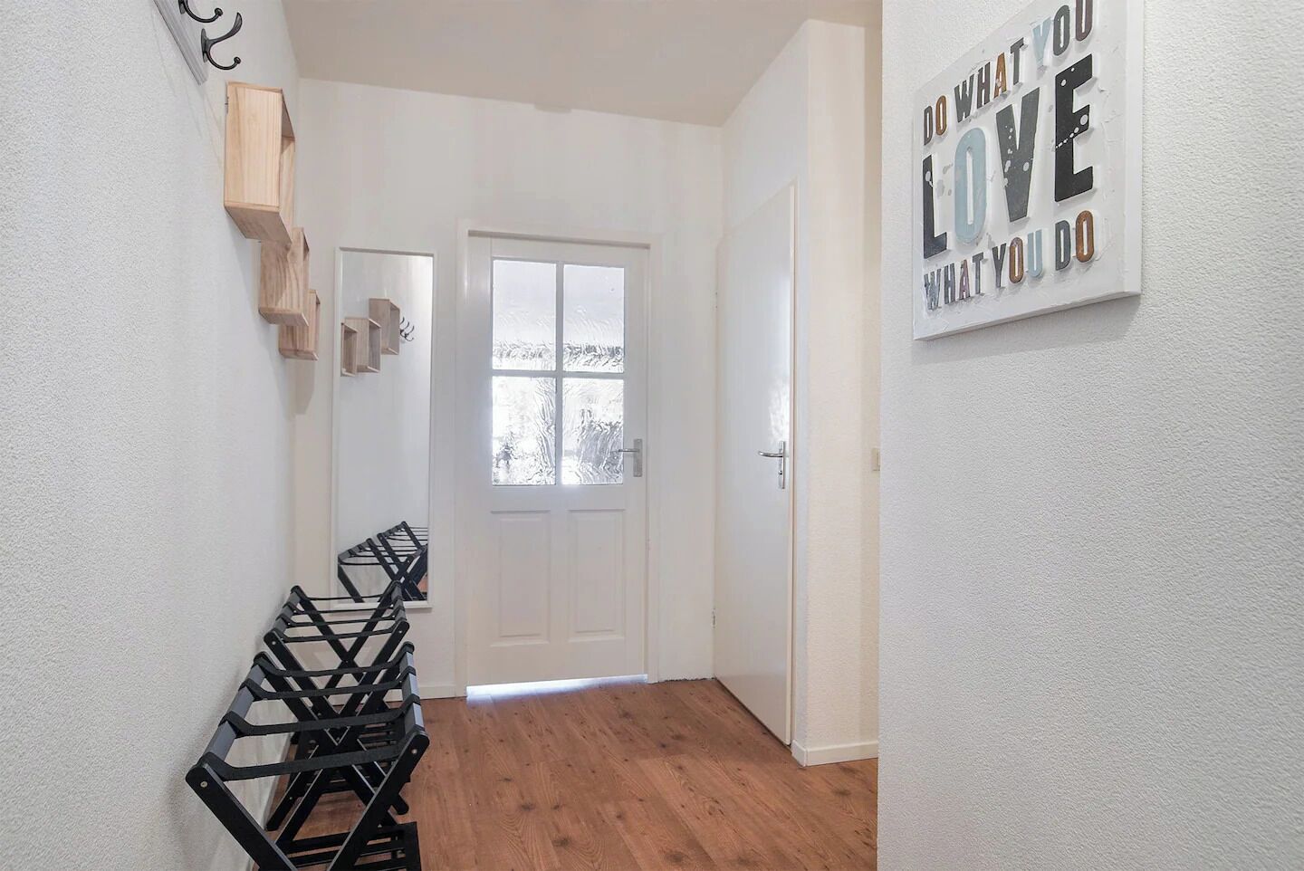 Un couloir avec un plancher en bois, une porte blanche et un panneau fixé au mur.
