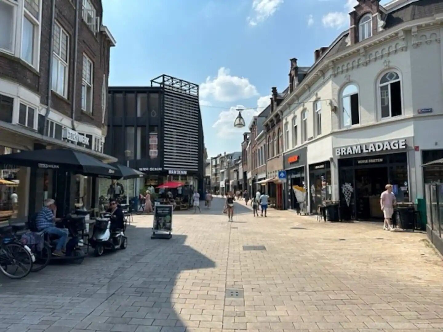 A cobblestone street with shops and cafes, including a visible 'BRAM LADAGE' store.