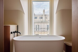 A modern bathroom with a freestanding bathtub, a window with a view of buildings, and a wooden vanity. - HIGHSTAY Maisons - Vintimille (Paris)
