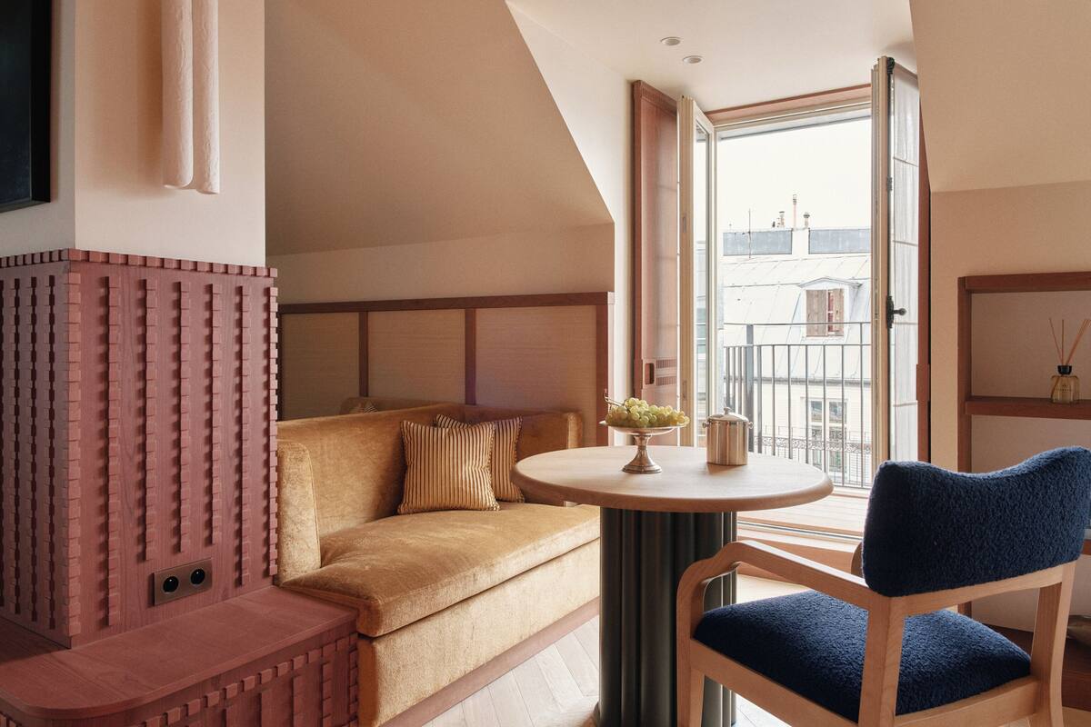 A modern living room with a sofa, a round table with a vase of flowers, and a view of the city through a large window.