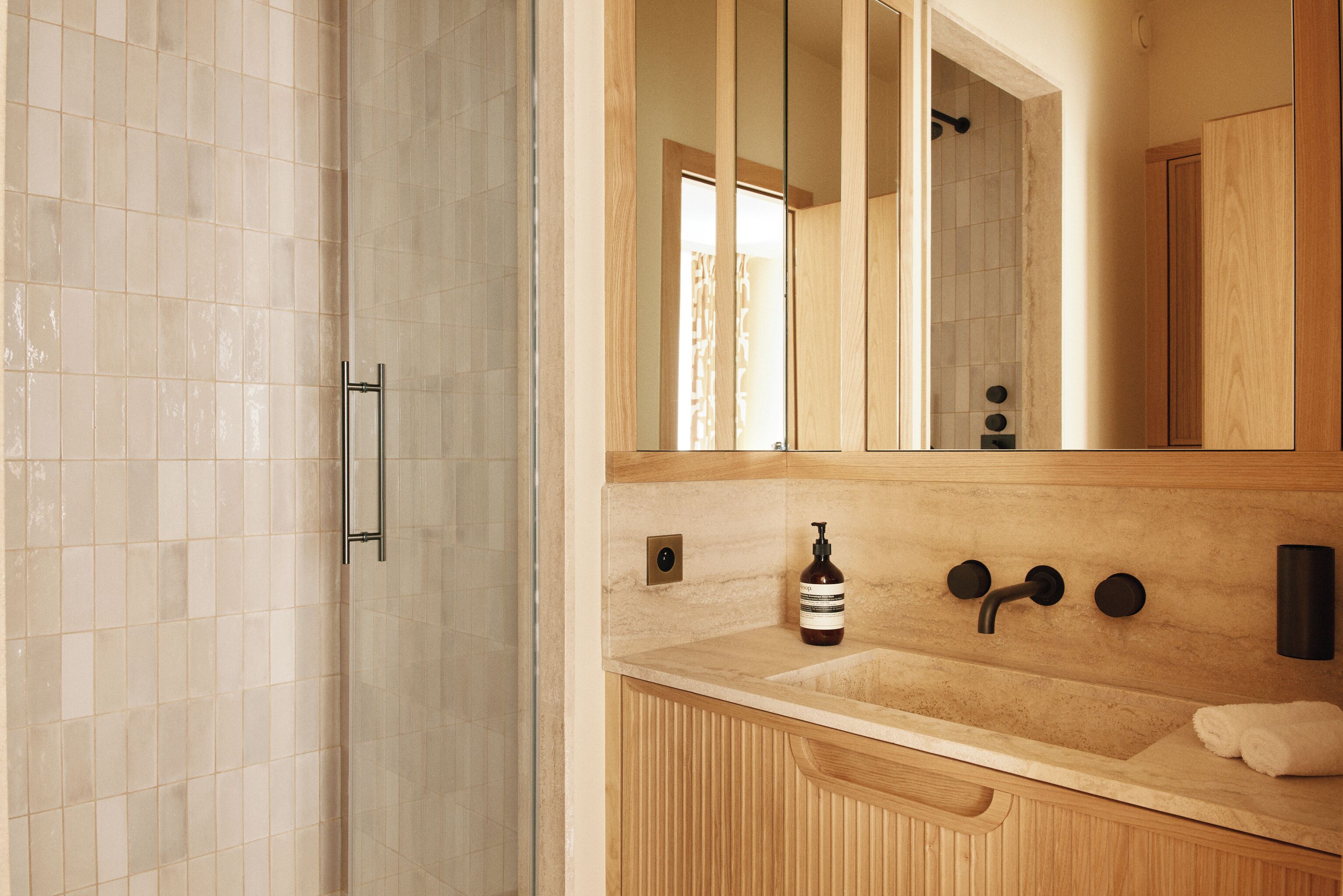 Ein Badezimmer mit gefliestem Duschbereich, einem Holzkosmetikschrank mit Waschbecken, einem Spiegel und einem Handtuchhalter.