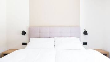 A neatly made bed with white linens, a light-colored headboard, and two black bedside lamps on either side.